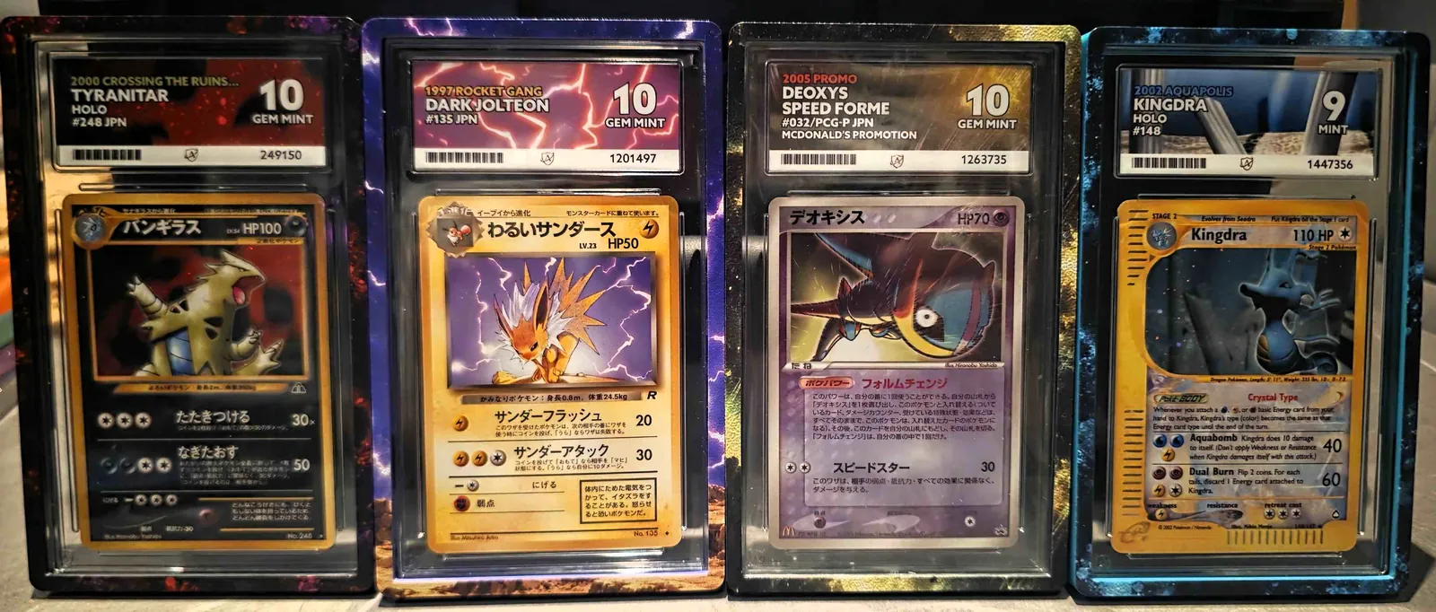 Four Ace Grading slabs in SlabCraft Full Art guards: Tyranitar, Dark Jolteon, Deoxys Speed Forme and Kingdra, each with the card's artwork extending around the guard